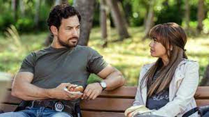 Wild Cards TV show screenshot: An Italian man wearing a police badge sits on a park bench talking to a Black woman.