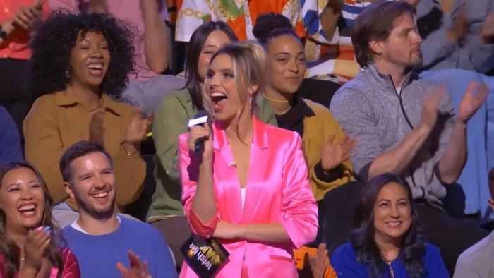 Wish List Games: Host Lele Pons stands in a bright pink suit in the studio audience.