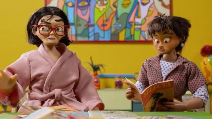 Women Wearing Shoulder Pads TV show screenshot 1: Marioneta, clad in a pink robe, sits at a table next to Coquita, who is reading a magazine. 