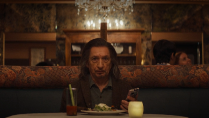 Wonder Man: Trevor sits at a restaurant table with a meal in front of him; he's holding his phone in one hand and appears stunned