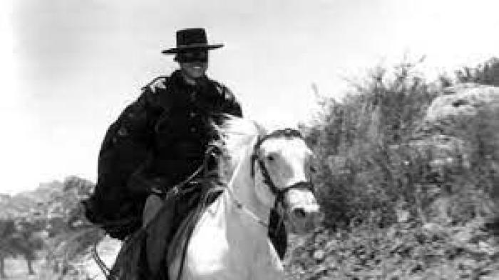 Zorro: a black and white shot of Zorro wearing a hat and mask while riding a horse.