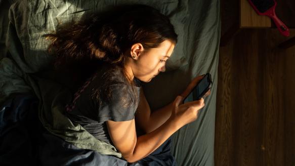 A girl lies in bed with a smartphone.