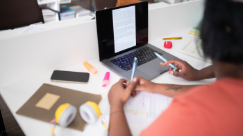 Person studying at desk with laptop, notes, and stationery.