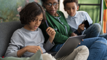 Family sitting on a couch, focused on a laptop and tablet.