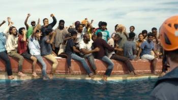 23 000 Lives movie: A group of people on a boat celebrate, with one person wearing an orange helmet in the foreground.