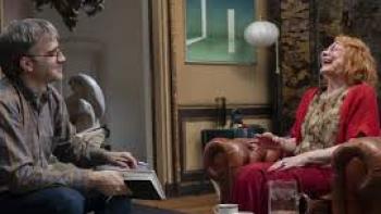 27 Nights Movie: Older woman laughs while talking with man in glasses