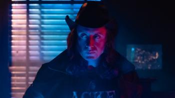5lbs of Pressure Movie: In a dark room, Mike (Rory Culkin), wearing a leather cowboy hat and a leather coat, looks sideways while bathed in pink and blue lights