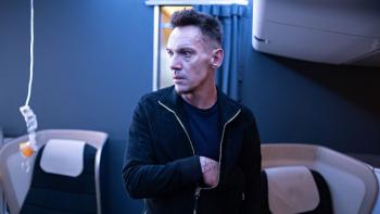 97 Minutes Movie: On an airplane, Alex (Jonathan Rhys Meyers) looks pensive as he reaches inside his coat; an oxygen mask hangs over a first-class sea