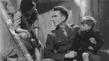 A Canterbury Tale: John Sweet sits with a young boy on his lap, talking to another boy on a ladder holding a makeshift gun