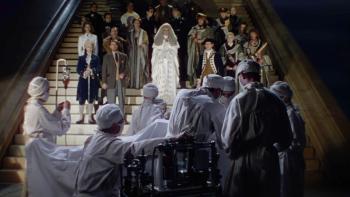 A Matter of Life and Death: Numerous historical figures stand on a staircase, with people in performing an operation below