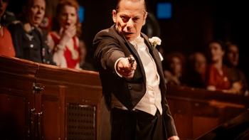 A Private Life movie: Wearing a tuxedo, Mathieu Amalric stands on stage pointing a gun, while the audience gasps