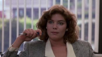 The Accused: Kelly McGillis sits holding a pen in an office, a window with vertical blinds behind her.
