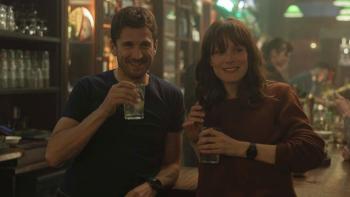 Ad Vitam movie: White French man left and White French woman right stand together smiling with drinks in hands in crowded bar