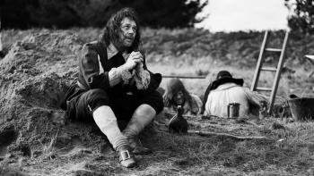 A Field in England: A man in 1600s English clothes sits on the floor and pleads with his hands together