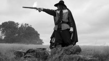 A Field in England: A man in 1600s British clothes fires a gun