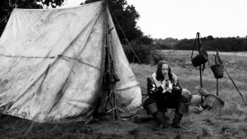 A Field in England: A man in 1600s English clothes and long hair sits outside a tent in a field