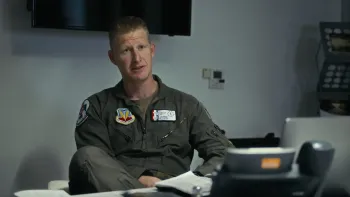 Air Force Elite: Thunderbirds movie: Lt. Col. Justin "Astro" Elliott sits in his office talking, center, wearing flight suit with badges 