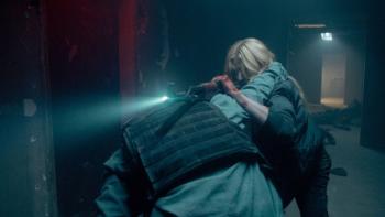 Air Force One Down Movie: Allison Miles (Katherine McNamara) fights with a terrorist in a dimly lit hallway; she uses a rifle fitted with a flashlight as leverage against his shoulder; his arm is around her neck