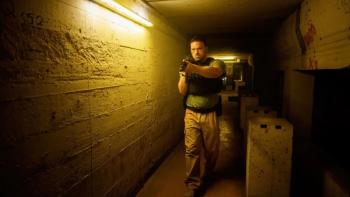 AKA: French White man in black bullet proof vest and khakis center walks down dimly lit tunnel with gun drawn 