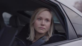 A woman looks out of the driver's side window of a car.