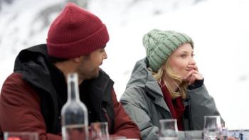 An Alpine Holiday movie: A man and a woman sit at an outdoor table together, with snowy mountains in the background