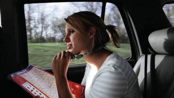 Megan Krizmanich sits in the back of a car holding a map. She is wearing a chunky necklace that she holds between her fingers.