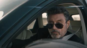 American Star Movie: Looking serious, Wilson (Ian McShane) sits in the driver's seat of his car, dark glasses pulled slightly down over his nose