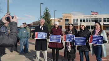 An American Pastoral movie: one man and four women stand holding school board voting signs for a picture op