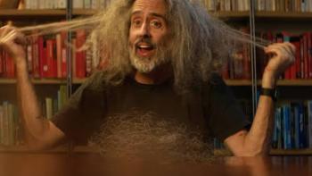Andre is an Idiot: Man with wild hair pulling it outward, sitting in front of a colorful bookshelf.