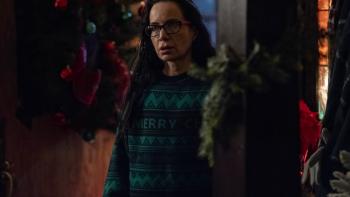 The Apology Movie: Gretchen (Janeane Garofalo), wearing a green holiday sweater, and with Christmas decorations all around, stands in the front entrance of Darlene's house
