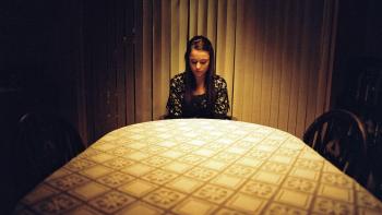 Apostasy: Molly Wright sits at the end of a dimly lit table, alone, looking down into her lap