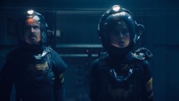 Ash Movie: Brion and Riya, wearing full spacesuits, explore the space station, looking tense and on guard
