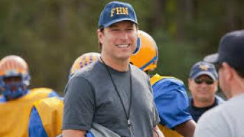 A Smile as Big the Moon: Football coach John Corbett smiling on field with players in gear.