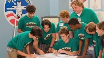 A Smile as Big the Moon: Group of students in green shirts collaborating on a project at a table.