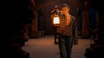 Baghead: A young blond White woman holding a lamp in a dark basement