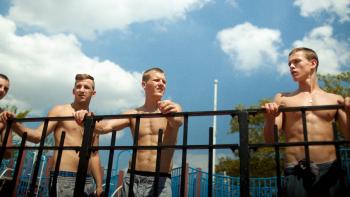 Beach Rats: Four young White men stand shirtless at a railing, overlooking the beach.