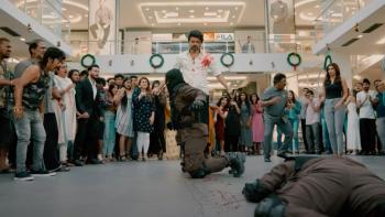 Beast: A middle-aged bearded Indian man with blood on his white shirt stands over two men he has just defeated in a fight while a crowd looks on