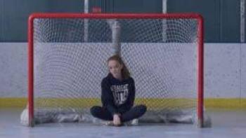 Before the Ice Melts movie: Girl sitting cross-legged in front of a red hockey goal net, wearing a navy sweatshirt.