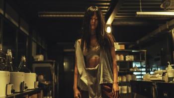 Believer 2 movie: Korean woman in bra and torn shirt center stands in a drug making facility