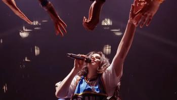 Billie Eilish Hit Me Hard and Soft movie: Eilish on stage, reaching for fans' hands, colorful lights in the background