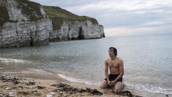 Black Dog: A shirtless White teen boy kneels on a beach