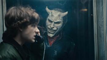 Black Phone 2 Movie: Finney (Mason Thames) talks on the phone in a booth, while the Grabber peers at him through the glass
