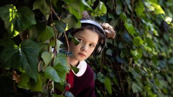 Blaze Movie: Twelve-year-old Blaze (Julia Savage), wearing headphones, hides behind a bush and peeks out at something