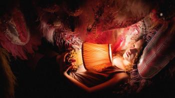 Blaze Movie: Blaze (Julia Savage), holding a small table lamp, curls up in the lap of her imaginary puppet dragon, Zephy