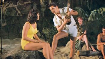 Blue Hawaii: Elvis Presley leans down to sing to Joan Blackman who sits on a log at the beach
