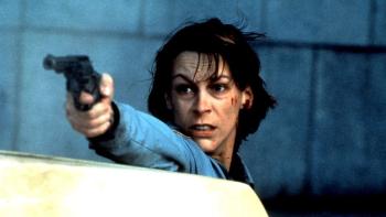 Blue Steel: Jamie Lee Curtis stands behind a car and holds a gun out in front of her, with blood on the side of her face