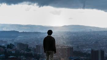 Bogota: City of the Lost movie: Korean man in jacket stands on hill looking out at the cityscape, buildings, and hills of Bogota, Columbia