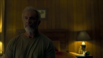 Boneyard movie: Mel Gibson in t-shirt left sits on bed in small bedroom, lamp and headboard behind him