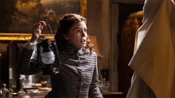 Borley Rectory — The Awakening: An older White woman in 1900 clothing looks frightened as she holds a lantern aloft inside an old manor house