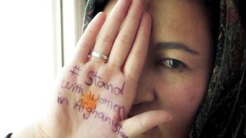 Bread & Roses movie: Afghan woman center shows palm held up in front of her eye and mouth, and on her palm reads, "#Stand with women in Afghanistan"